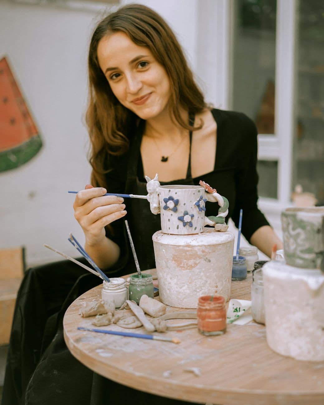 A ceramicist smiling as she paints a hand-thrown mug at her worktable