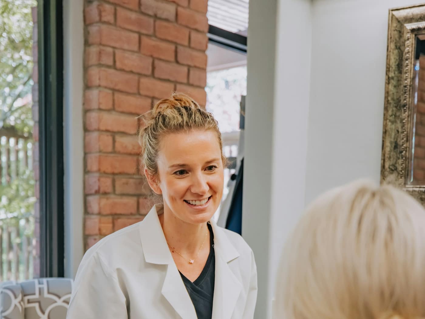A dentist in a white coat smiling as she talks a patient through the visit
