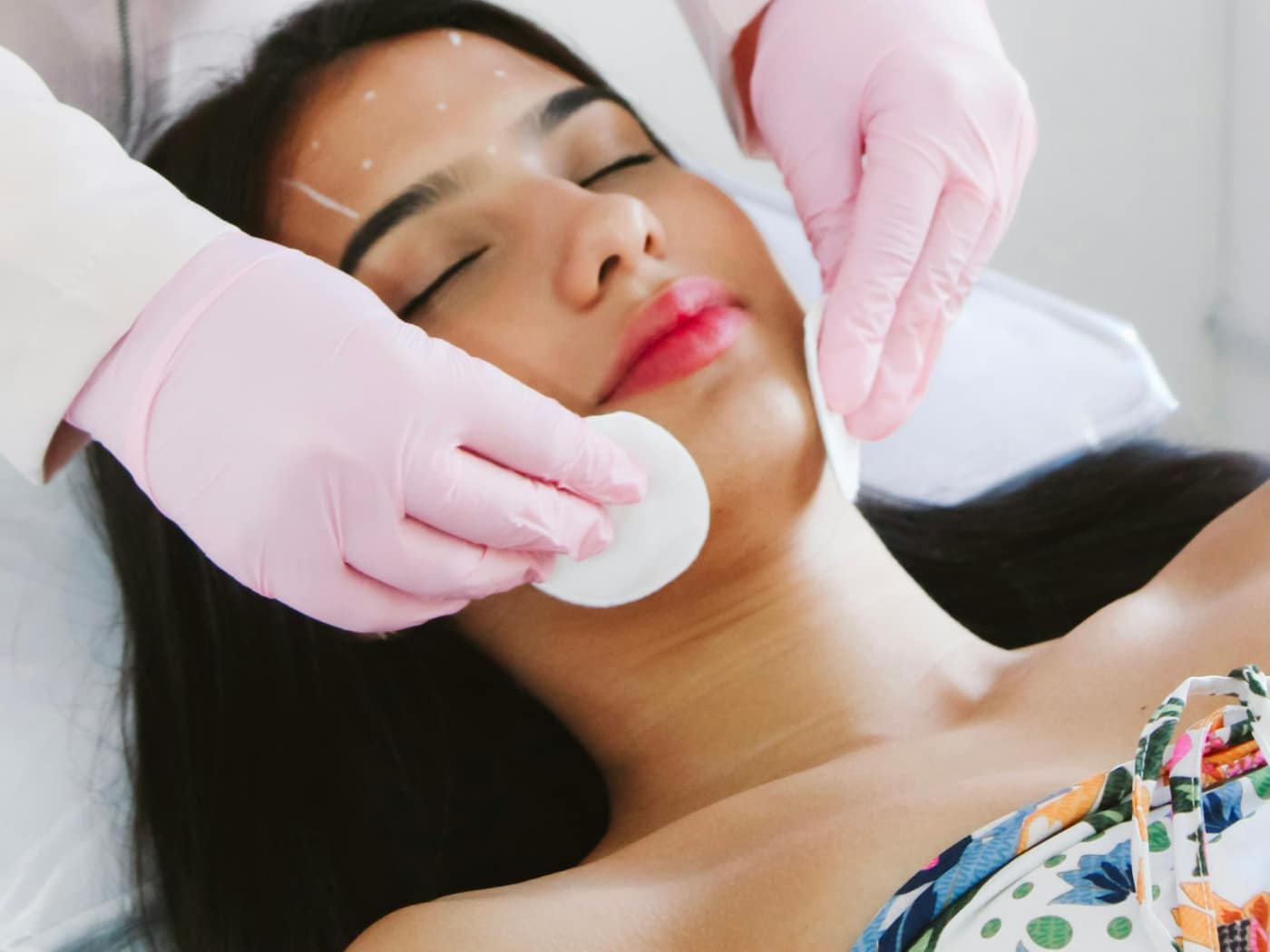 A skin specialist in gloves preparing a patient's face for treatment