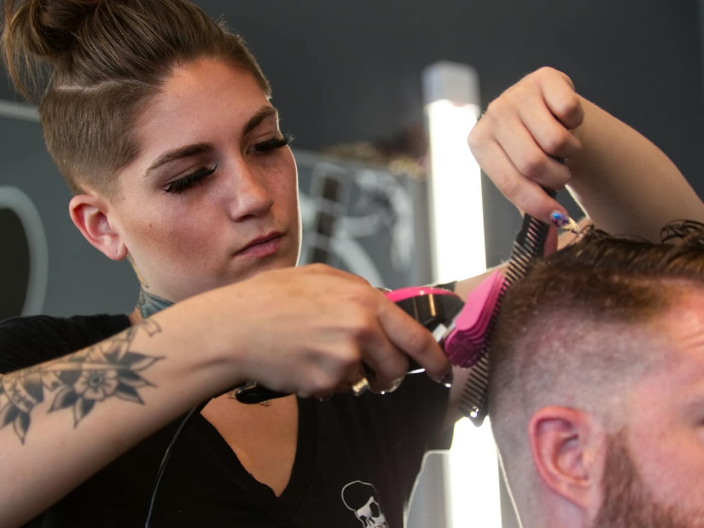 A tattooed stylist concentrating as she cuts a client's hair with scissors