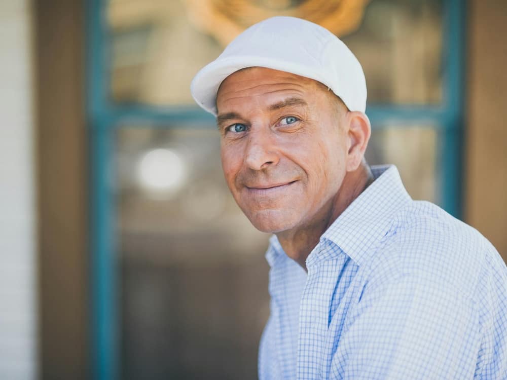 A smiling estimator in a white cap and checked shirt on a client's porch