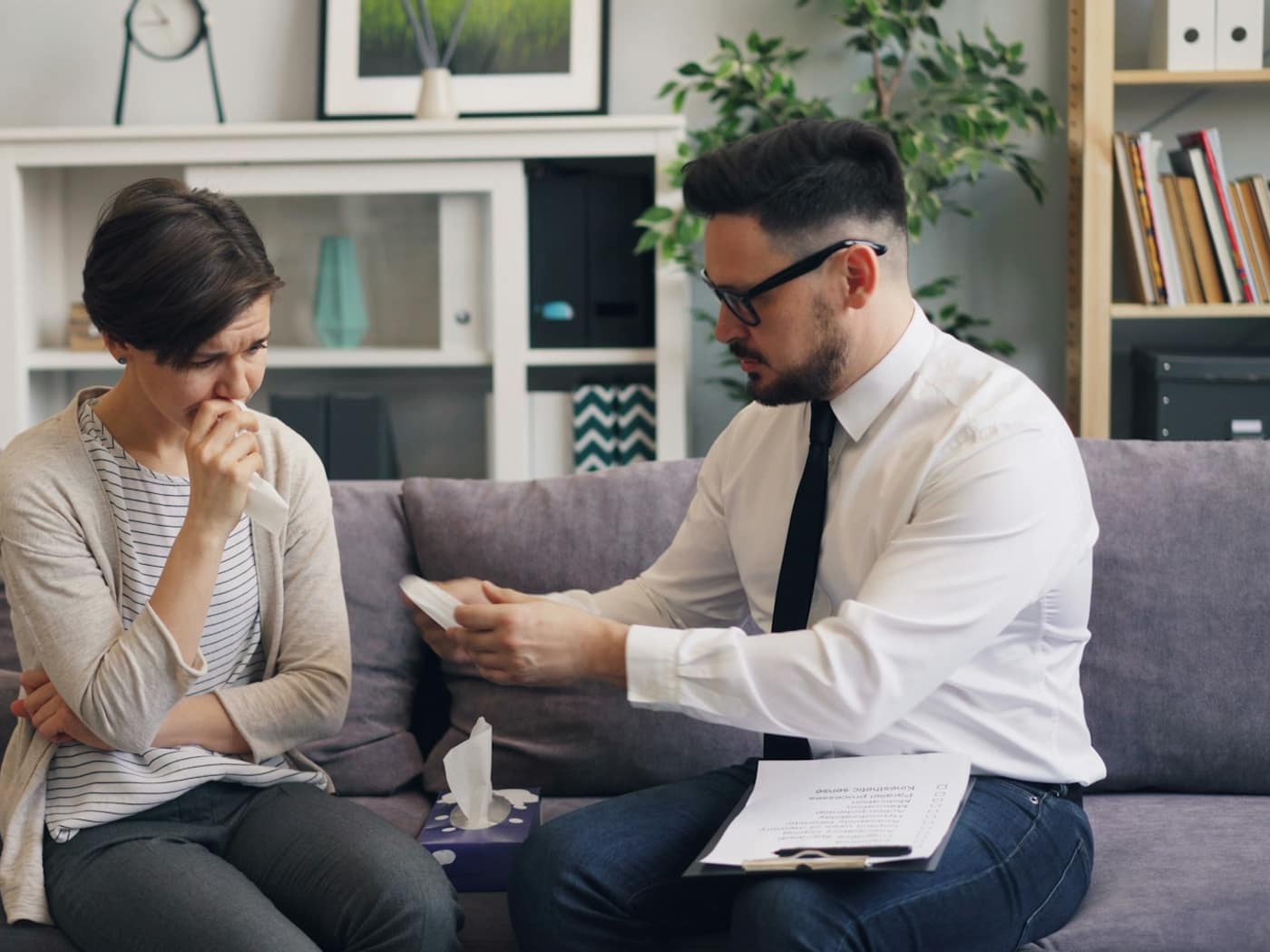 A lawyer reading through a client's papers with her on the sofa in his chambers
