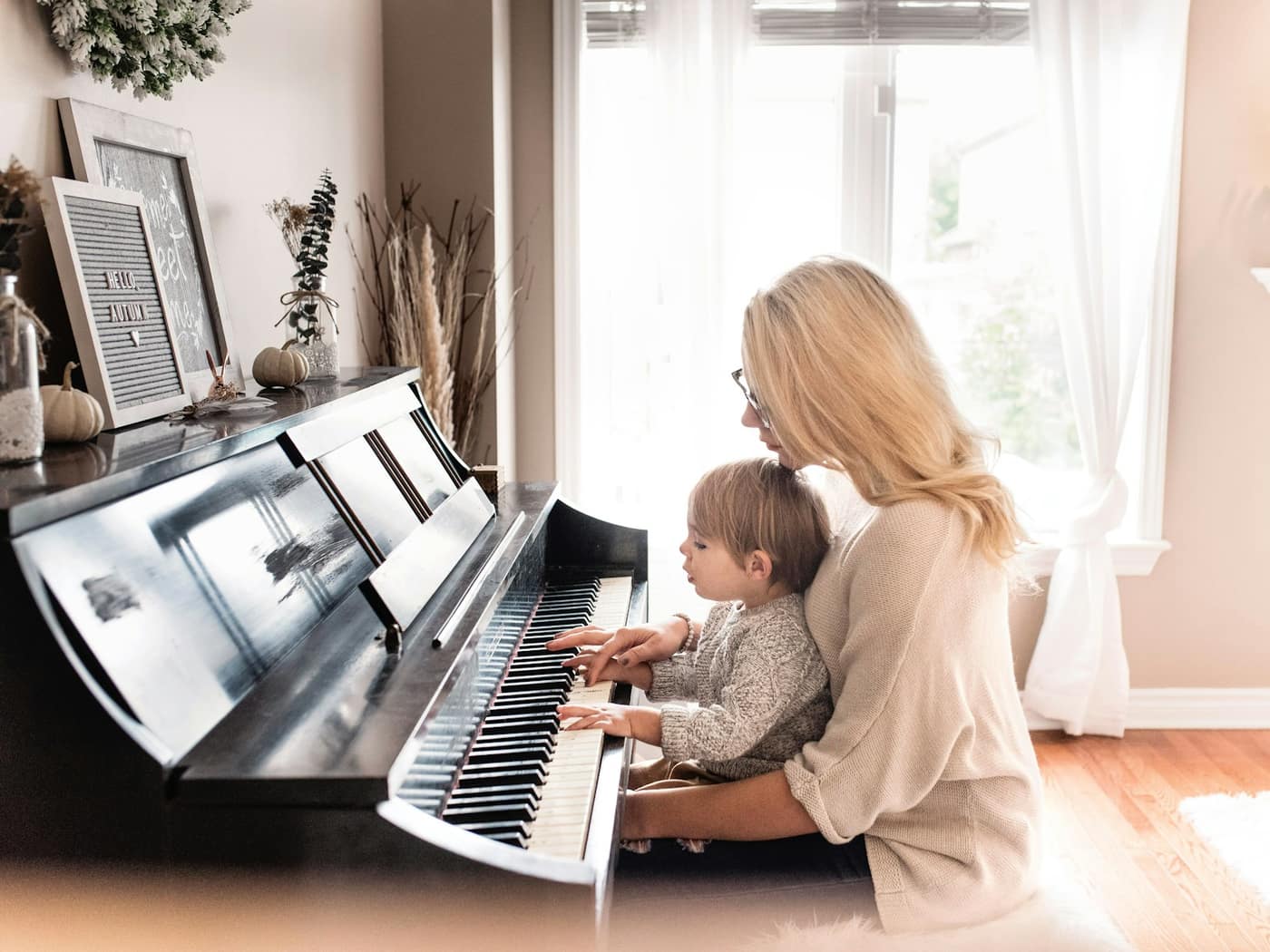 A piano teacher sitting with a young pupil at a digital piano in a sunny room