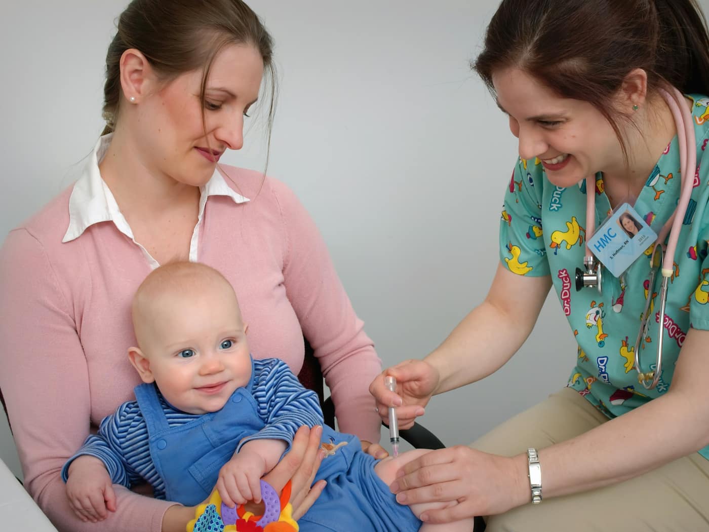 A paediatrician in bright scrubs examining a baby held by his mother