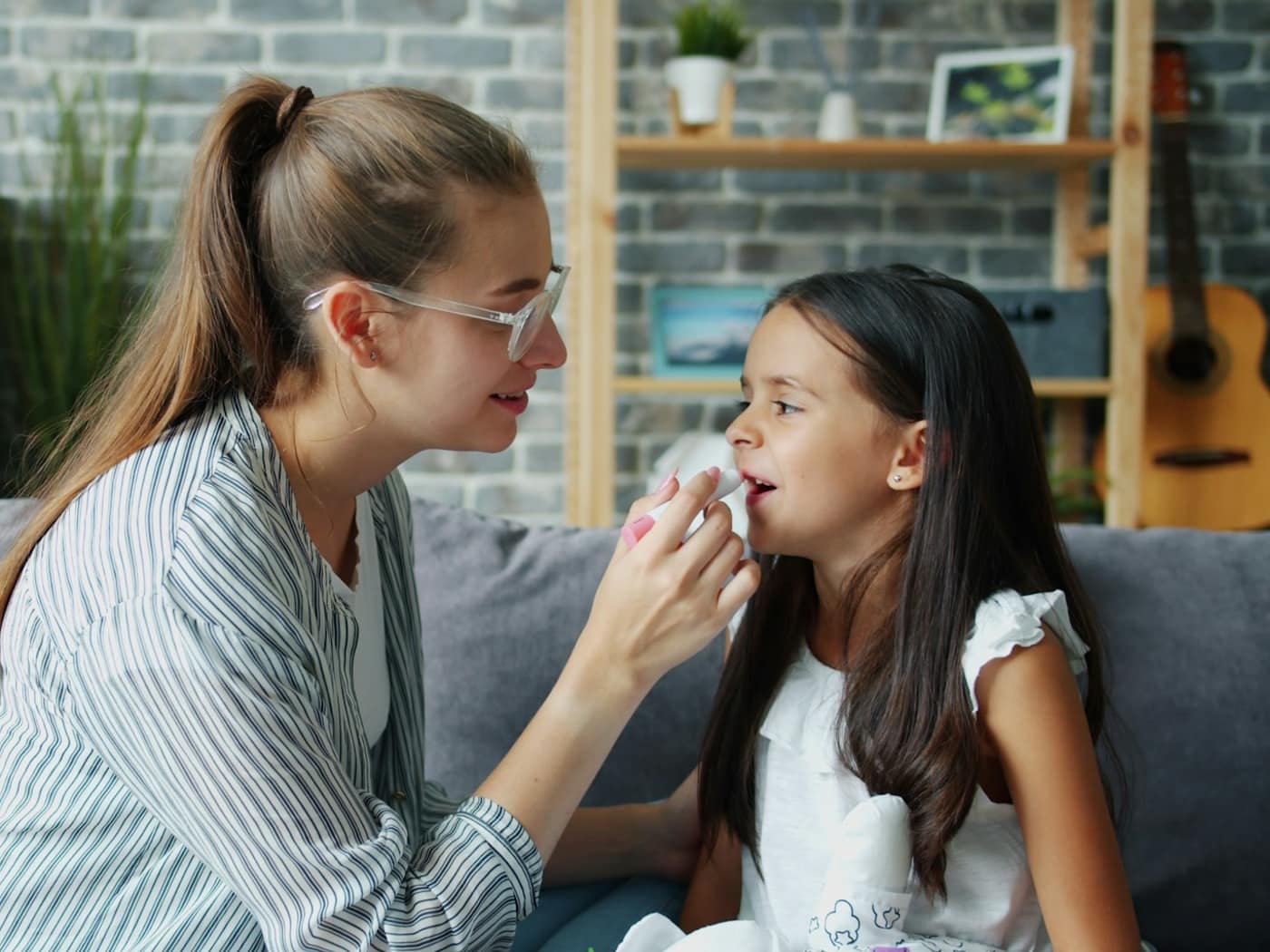A speech therapist guiding a girl's mouth position during a session on the sofa