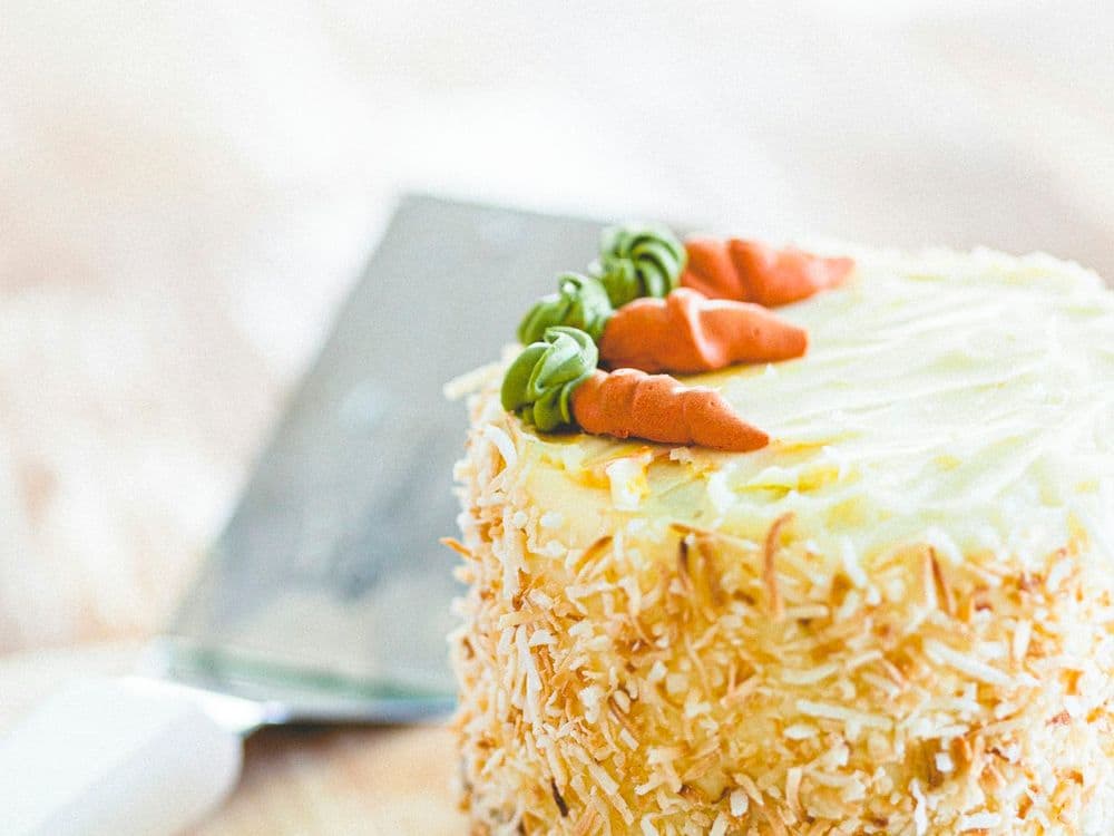 A tall frosted carrot cake covered in toasted coconut