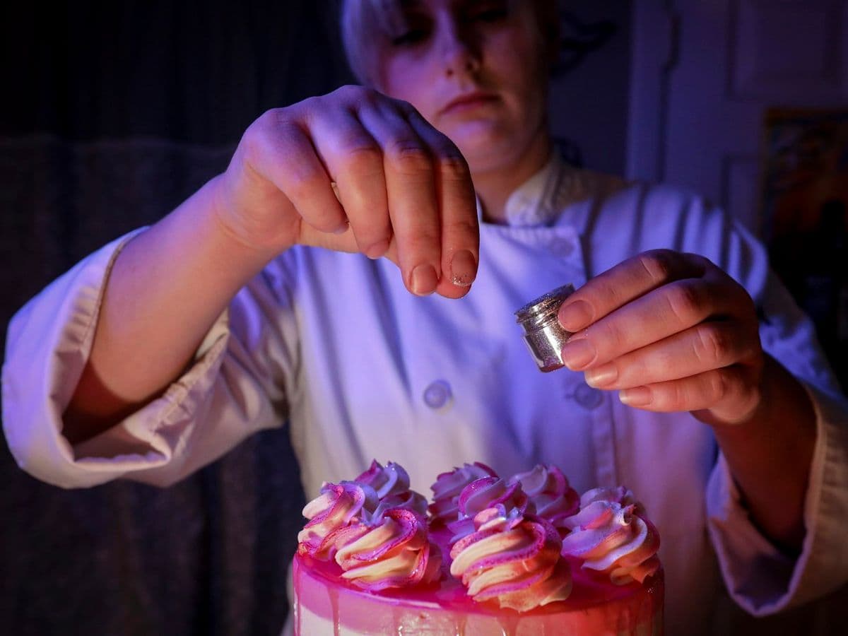 Gloved hands finishing pink cupcakes with a sprinkle