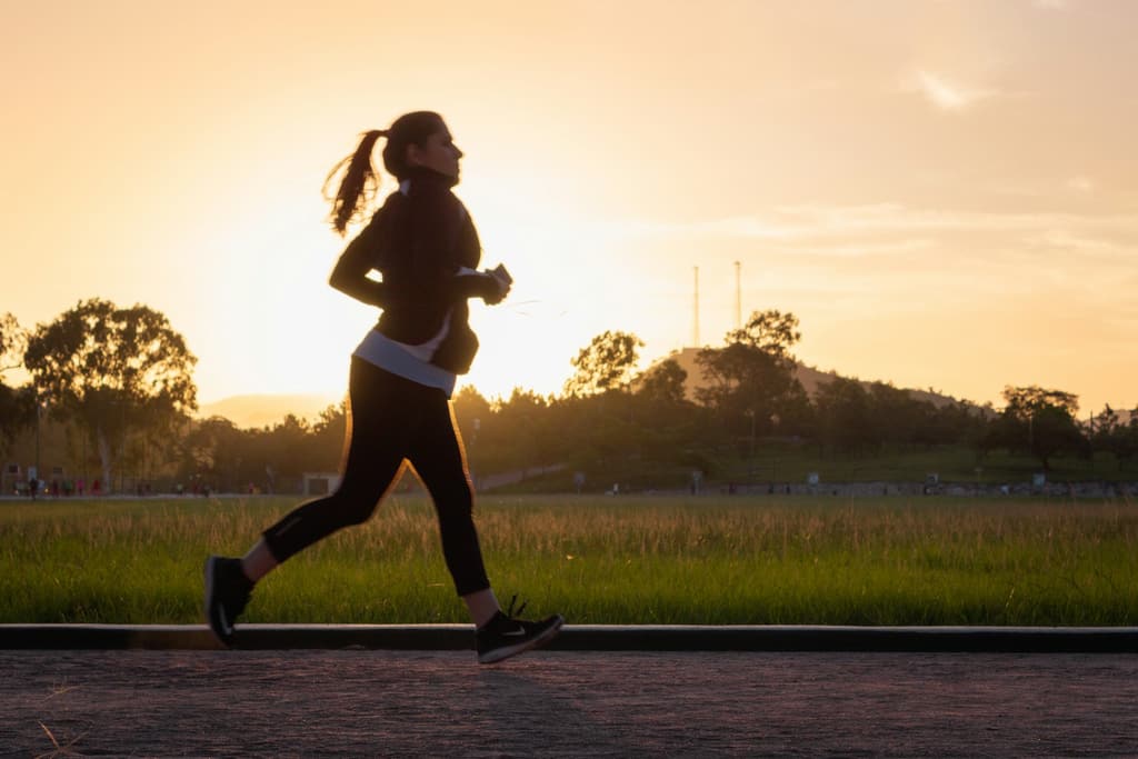 A woman jogging along a park path at sunset