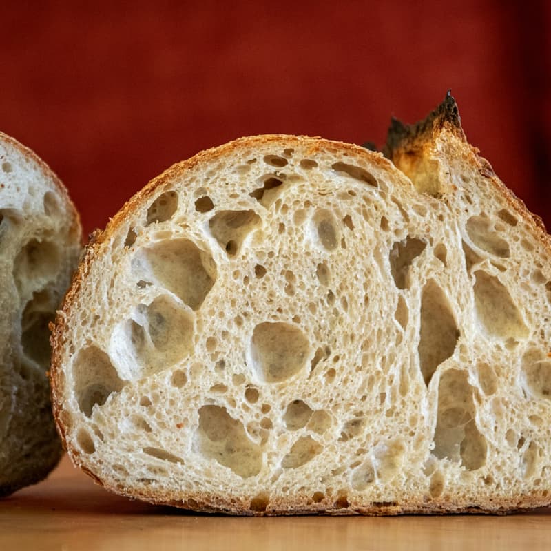 A baked sourdough loaf with an open ear cooling on a rack