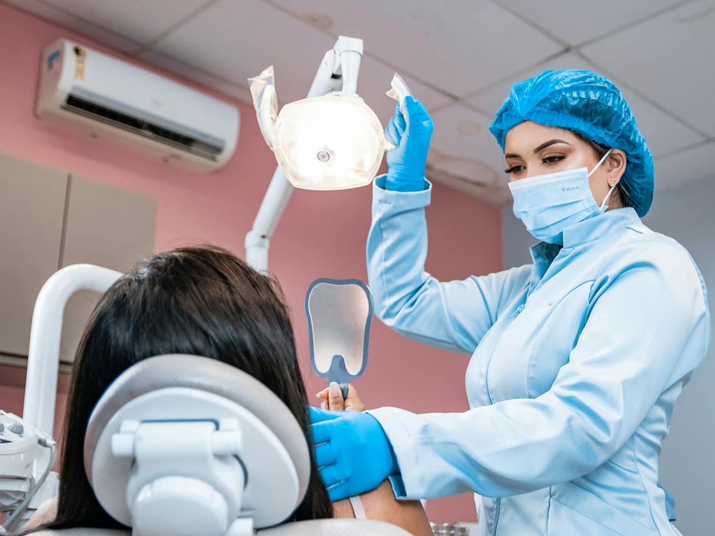 A dentist in a blue cap adjusting the light over a patient in the chair