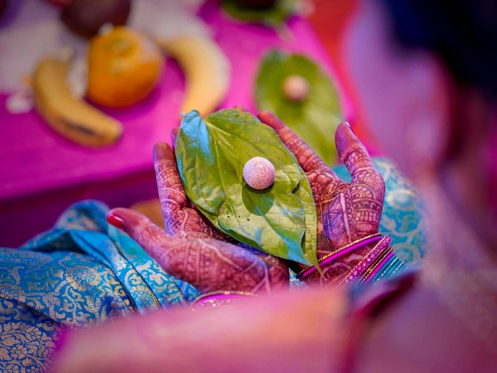 Hands holding betel leaves and a small offering during a wedding rite