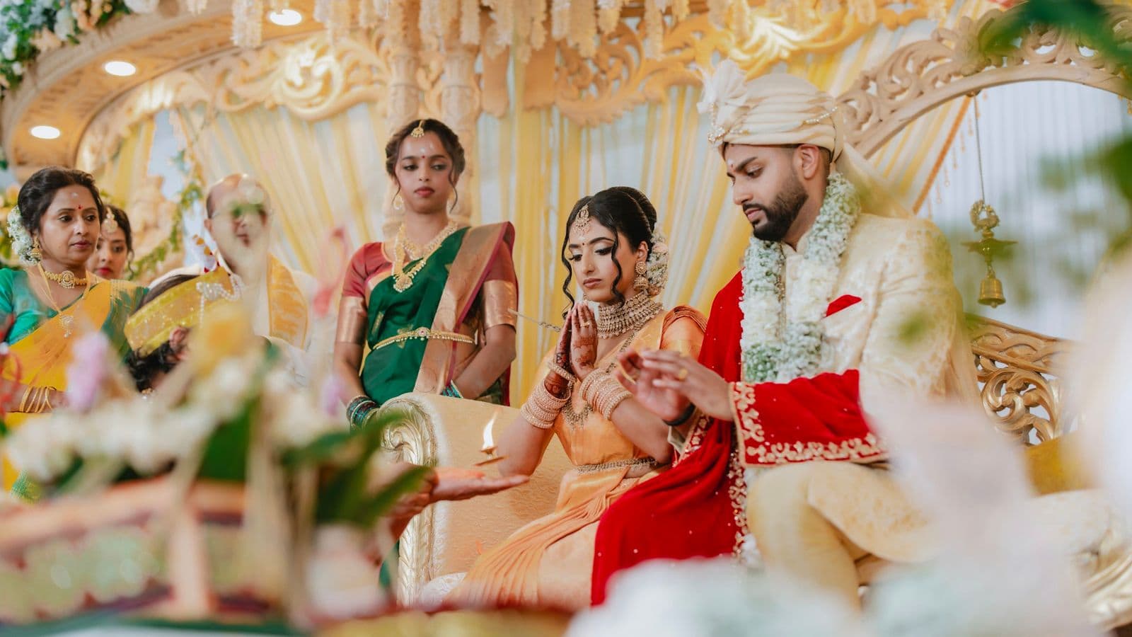 A bride and groom seated on a decorated stage with family around them during a wedding ceremony