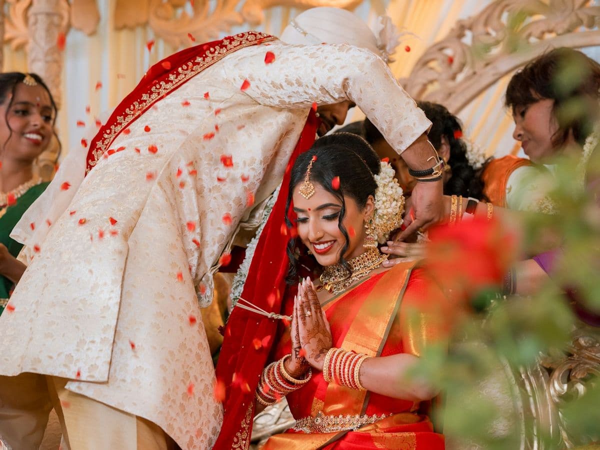 A bride with her hands pressed together as rose petals fall around her