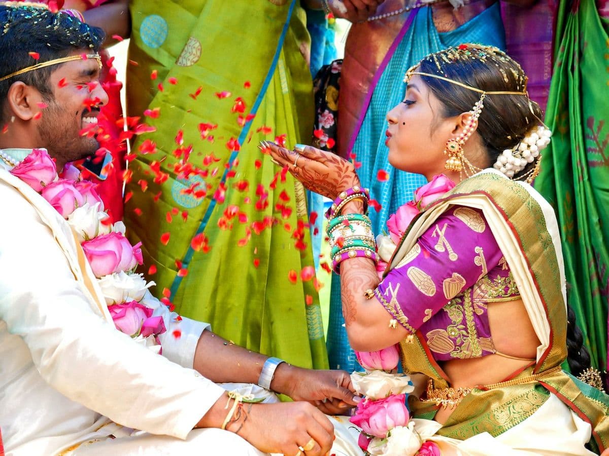 A bride and groom in garlands being showered with flower petals