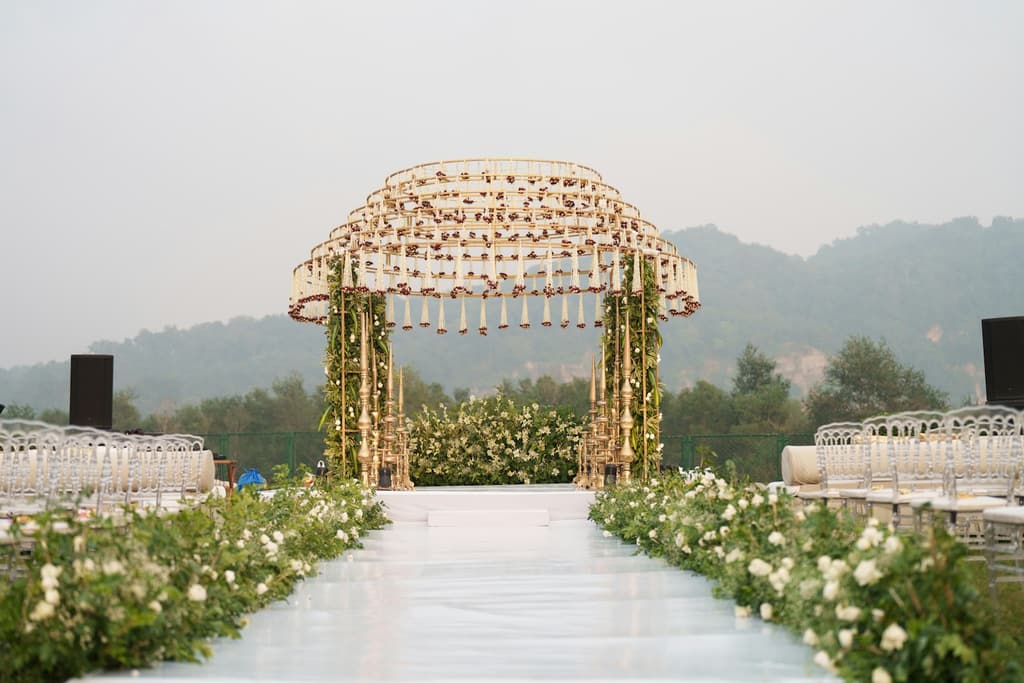 A floral wedding mandap set up at the end of an aisle with mountains behind