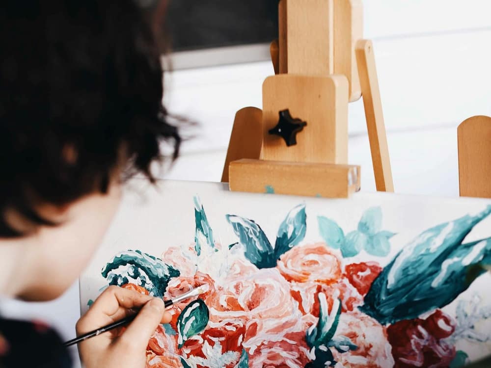 A hand painting pink roses on canvas with a thin brush