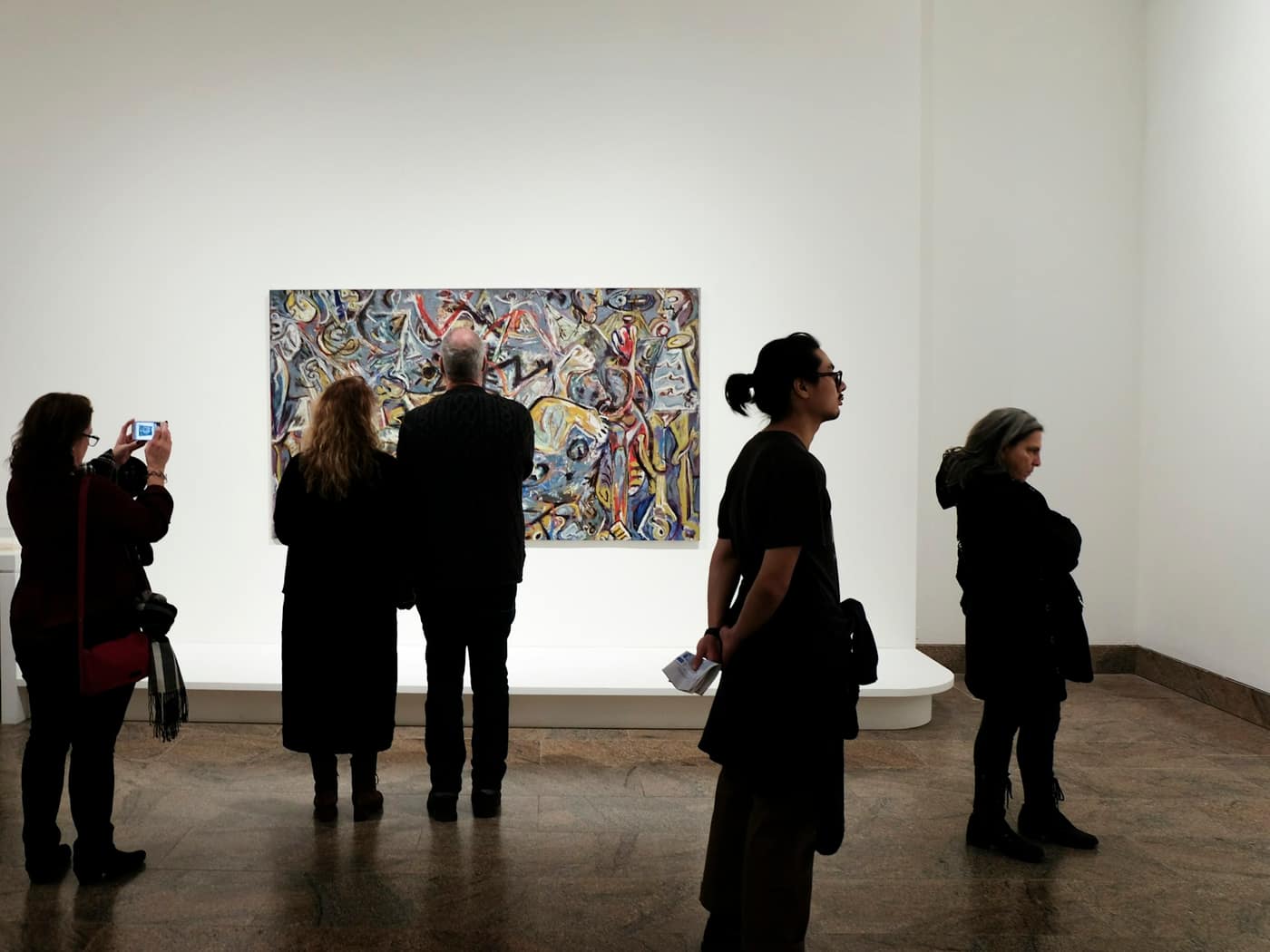 A small group of visitors standing in front of a colourful painting in a gallery