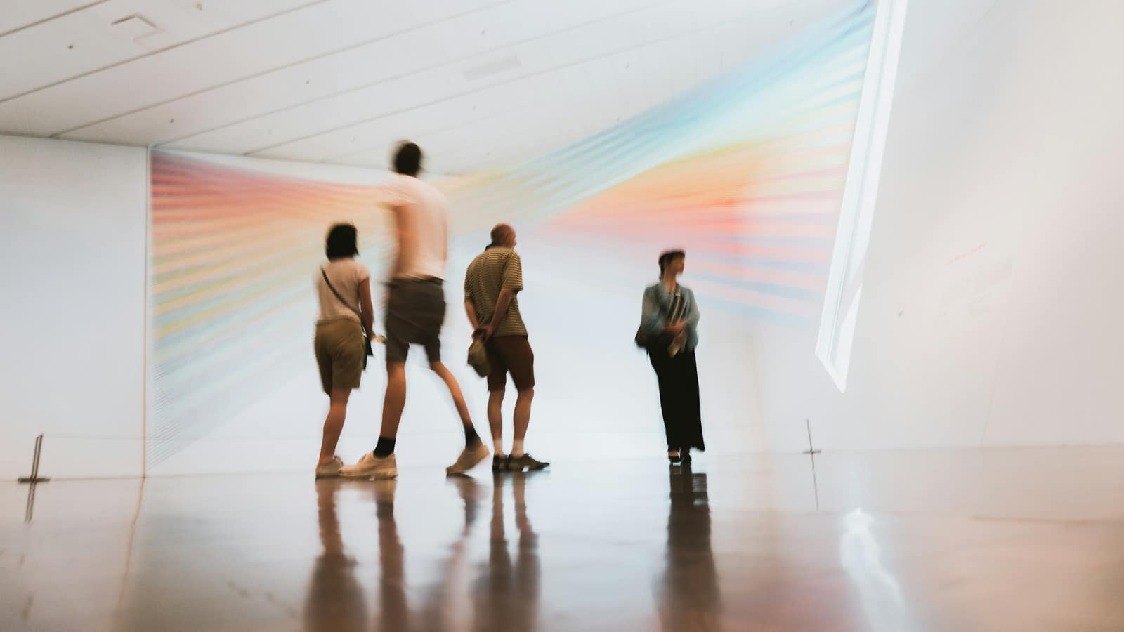Visitors walking through a bright white gallery towards a rainbow light installation