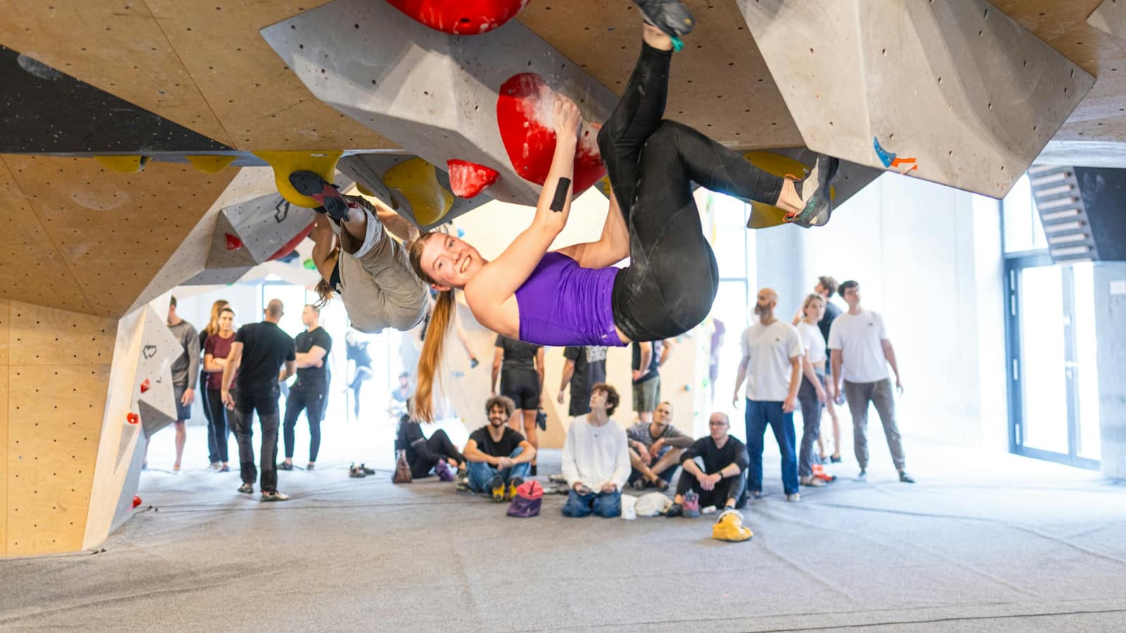 Climbers bouldering across an overhanging wall while a group of friends watches below
