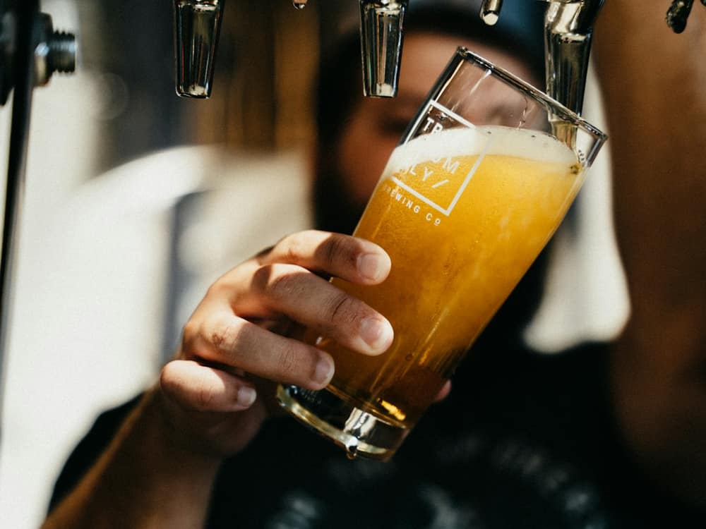 A hand holding a glass of hazy golden beer just poured