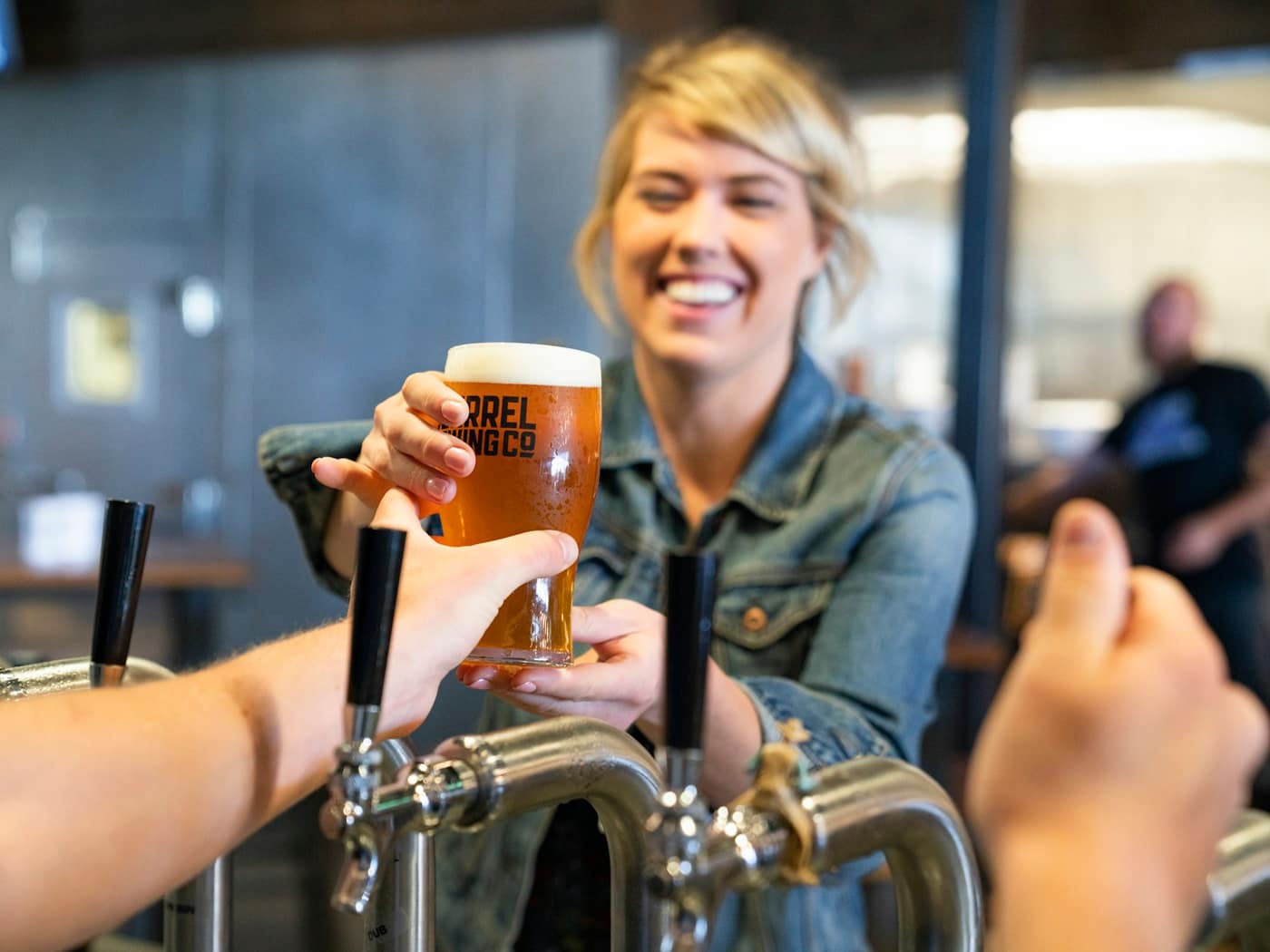 A woman smiling at the bar as a fresh glass is poured from the taproom's taps