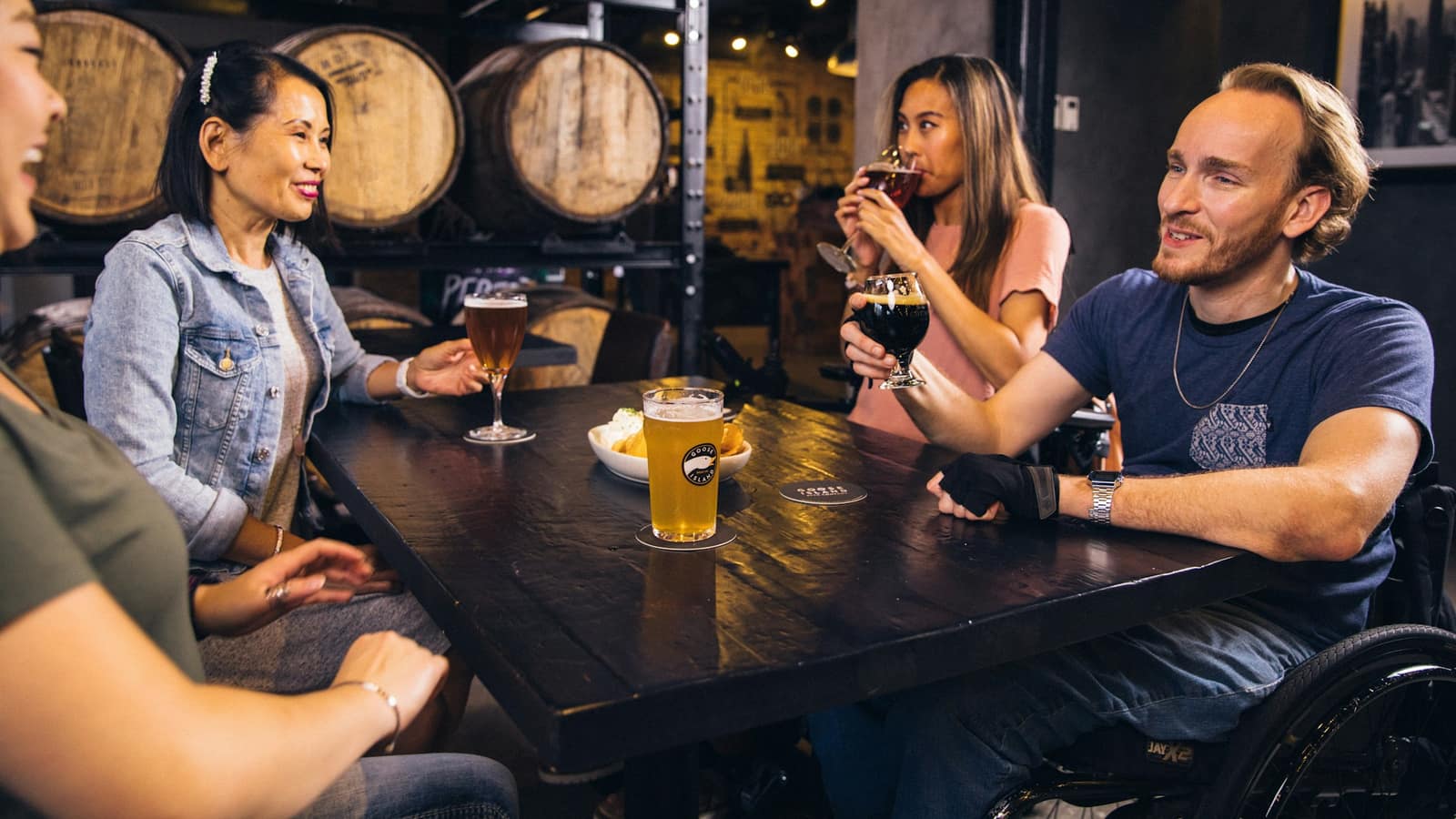 Friends sharing beers at a table in a cellar taproom lined with barrels