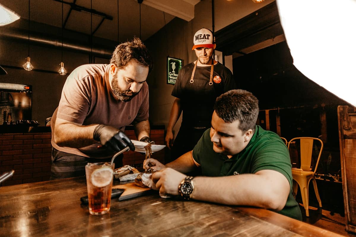 Two men talking over a wooden taproom table with a glass of beer