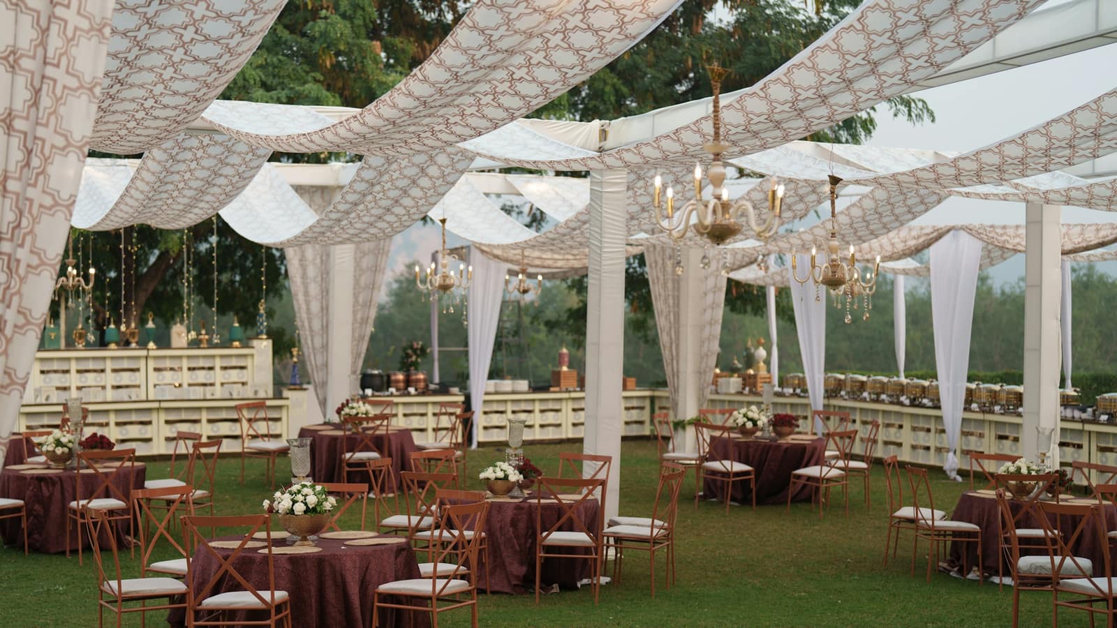 A garden lawn set with round dinner tables under white fabric canopies