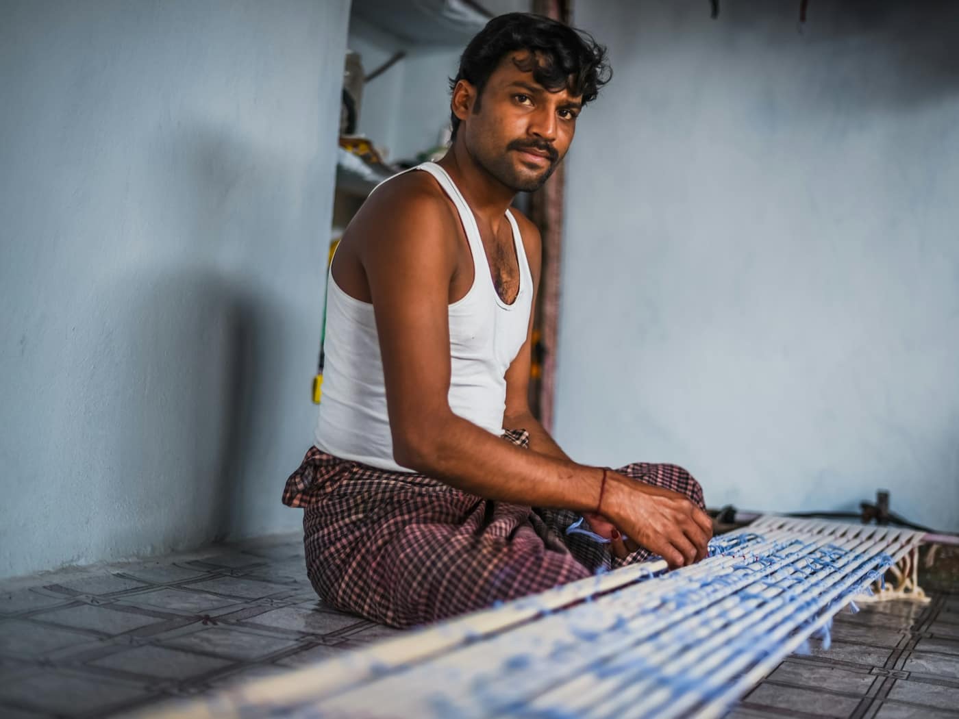 A weaver sitting on the floor at his handloom, smiling at the camera