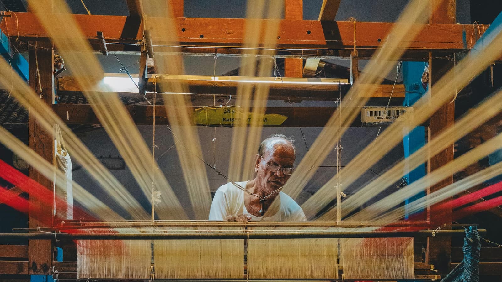 A weaver at a traditional loom with bright threads fanning out in front of him