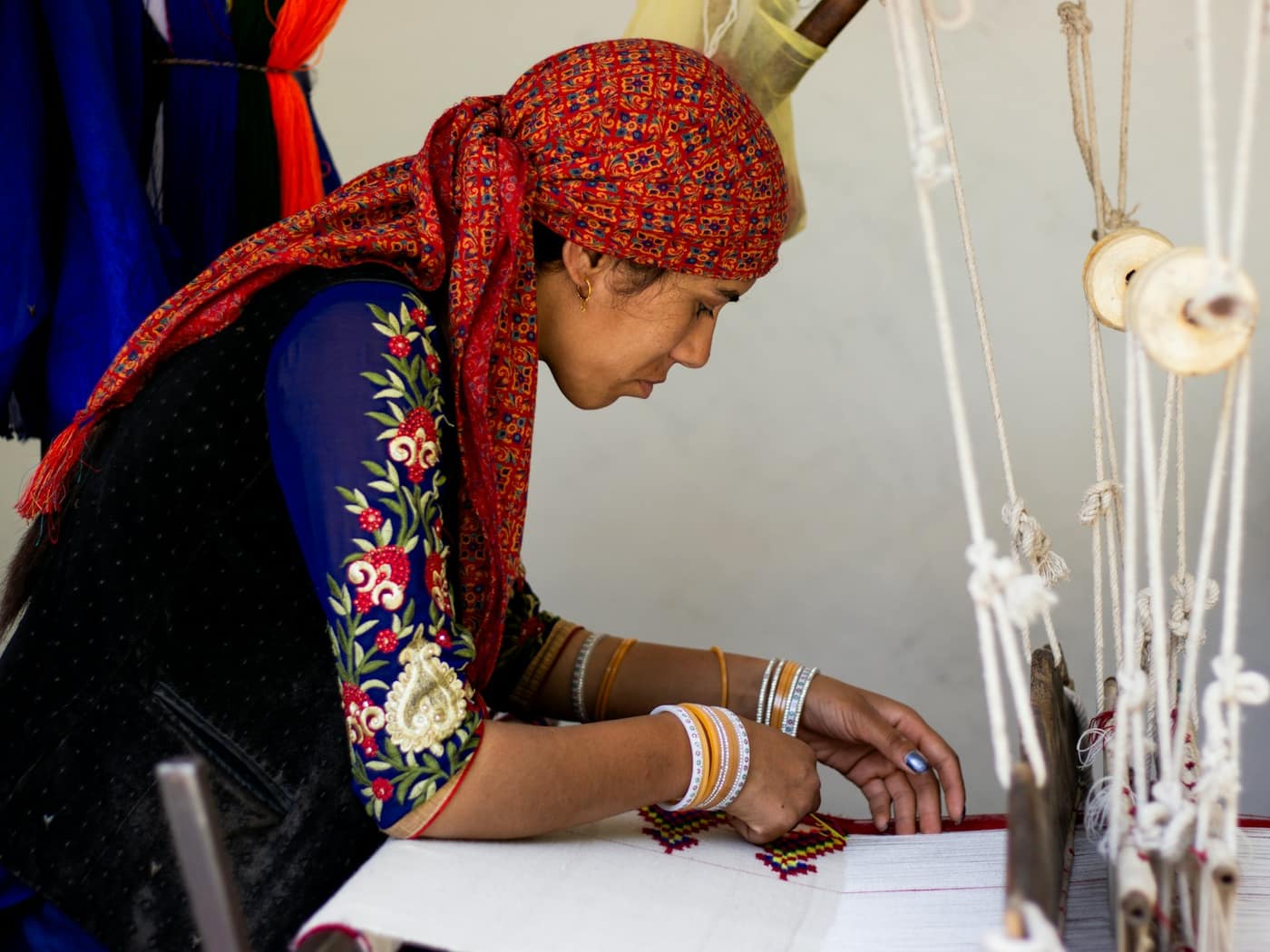 A weaver in a red headscarf working the threads of a handloom