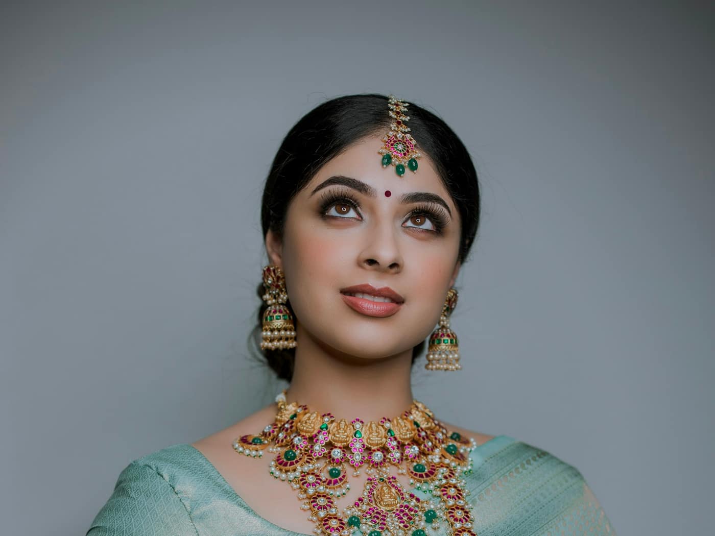 A woman in a green silk sari wearing a long temple necklace and jhumkas