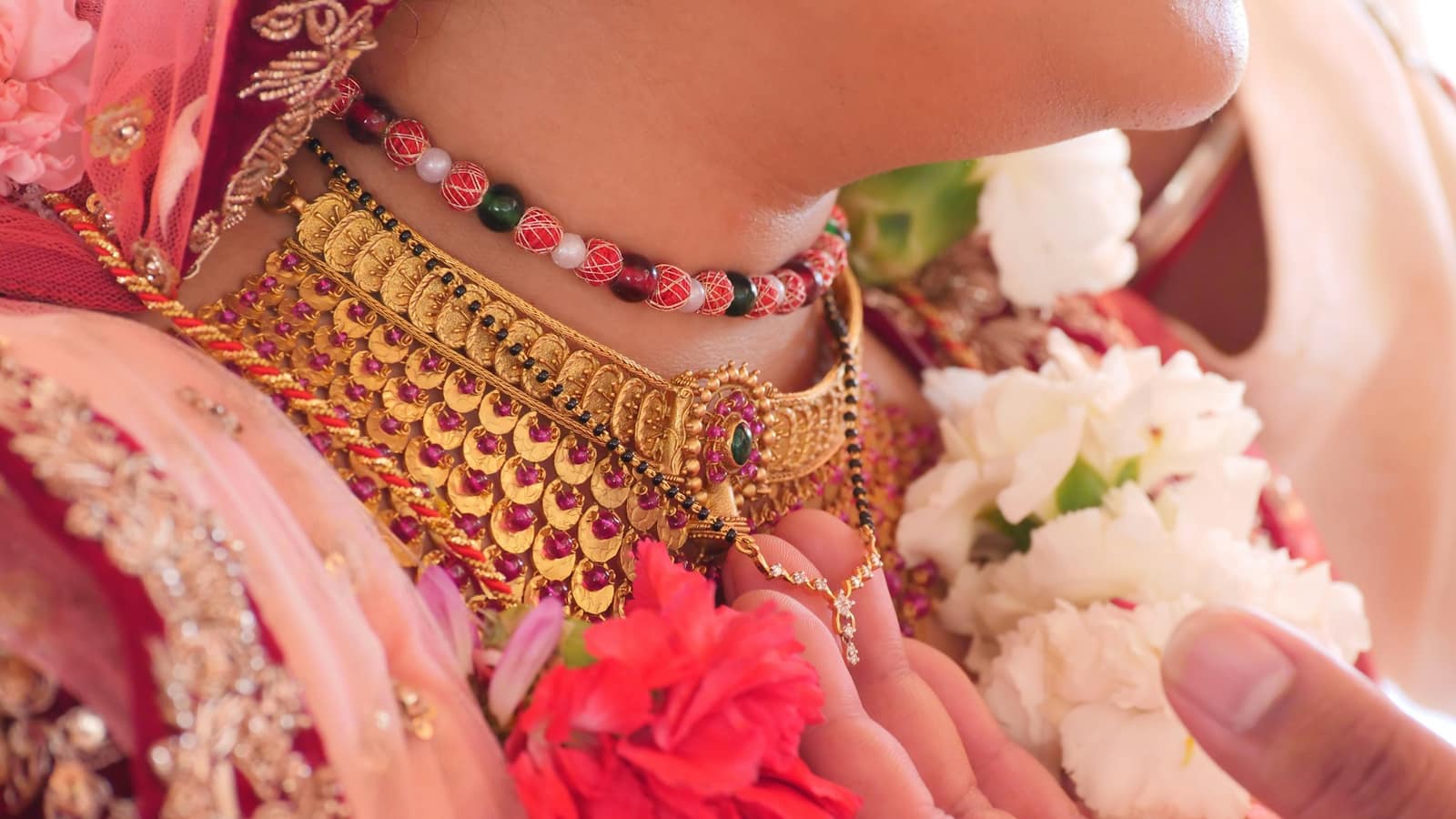 A bride's hands with gold bangles and a layered necklace among pink flowers