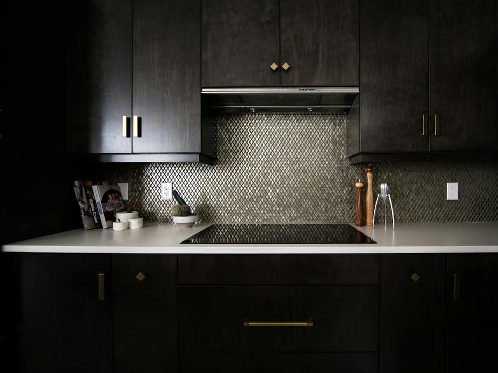 A dark cabinet run with a flush induction hob and a mosaic splashback