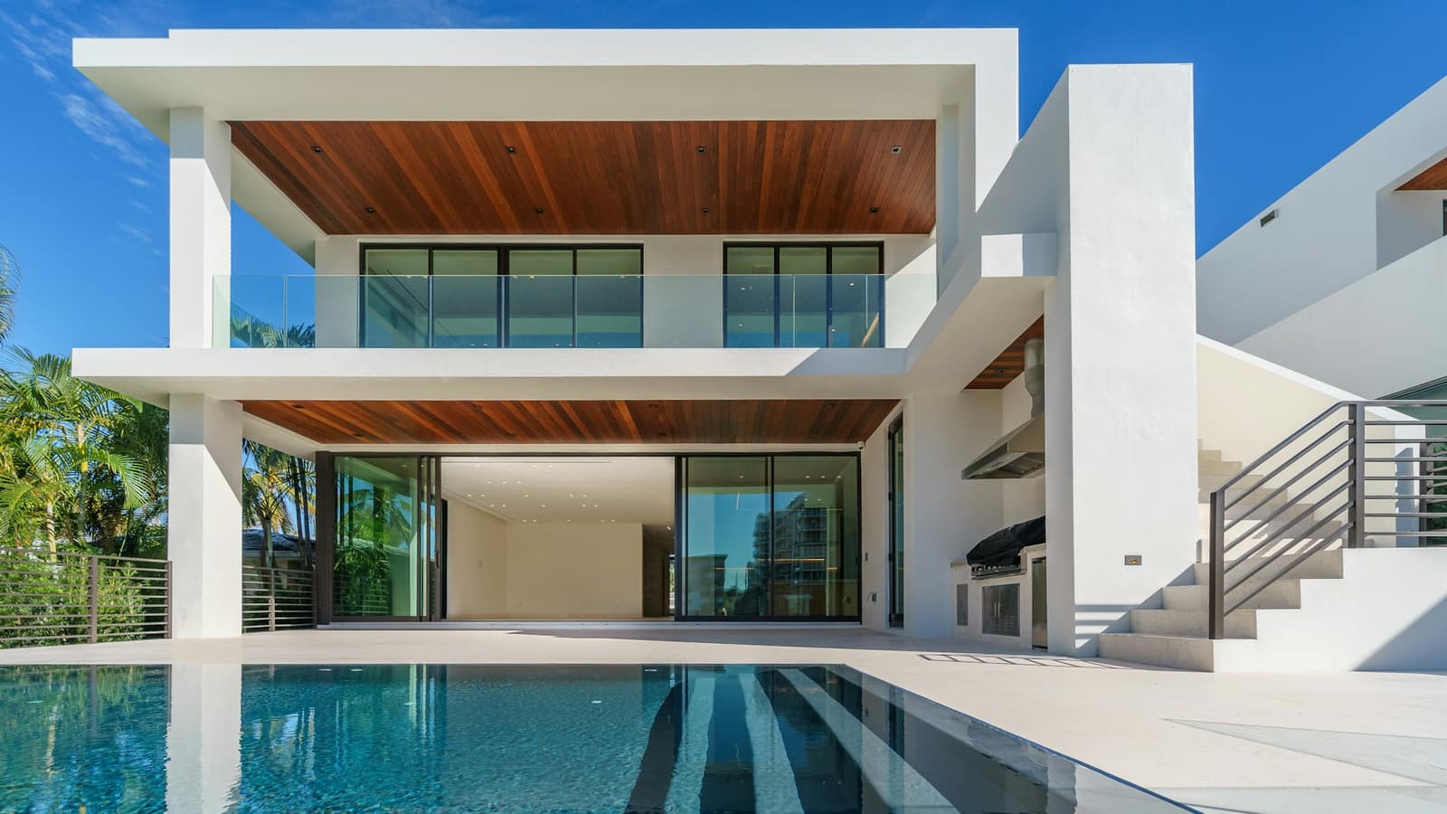 A white two-storey villa with a timber soffit behind a long pool