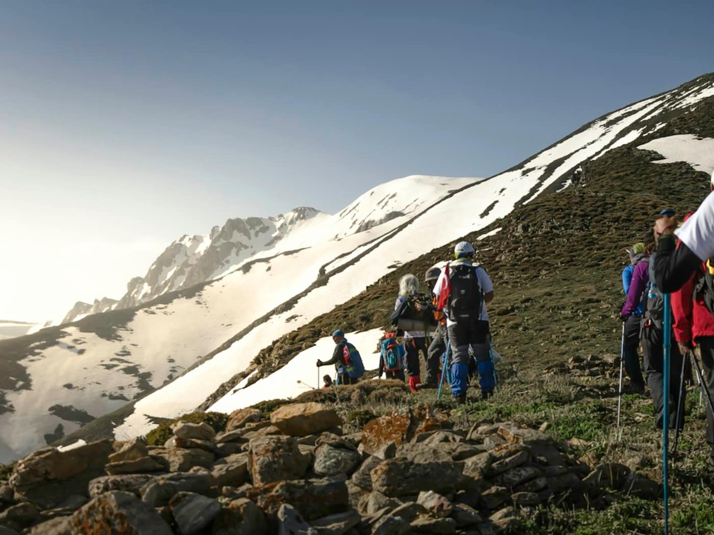 Trekkers in bright jackets climbing a snowy ridge on a mountain trail