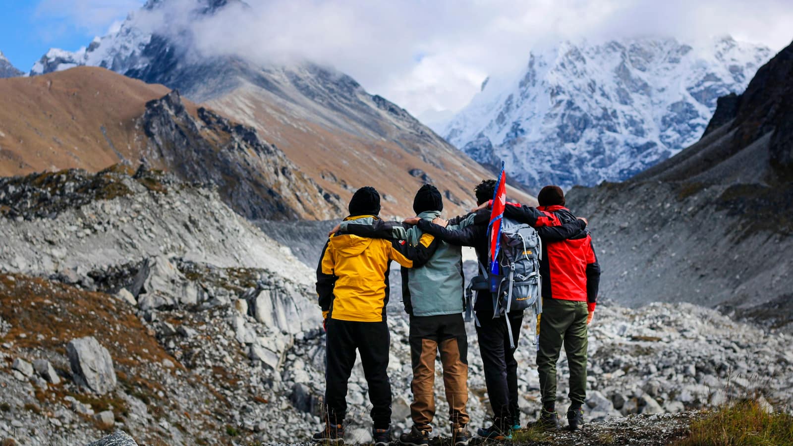 A group of trekkers with arms around each other on a high stony pass below snow peaks